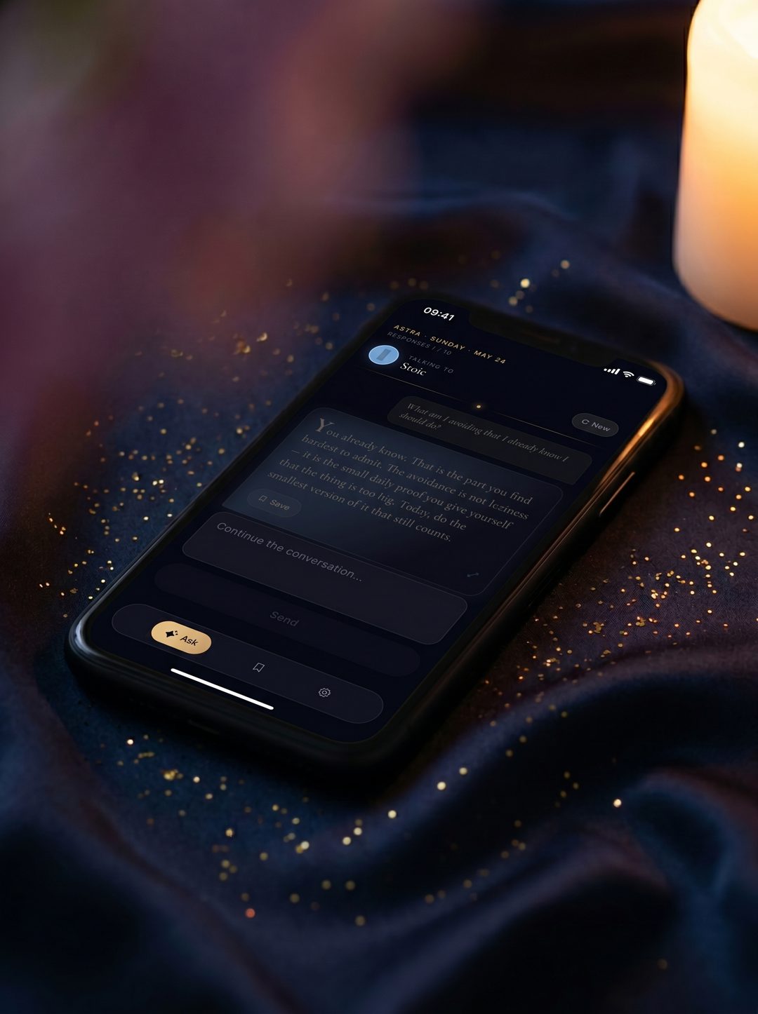 An iPhone on midnight-blue silk, candle warm light from the right, gold flecks scattered around. The screen shows a Stoic reading: 'You already know. That is the part you find hardest to admit.'